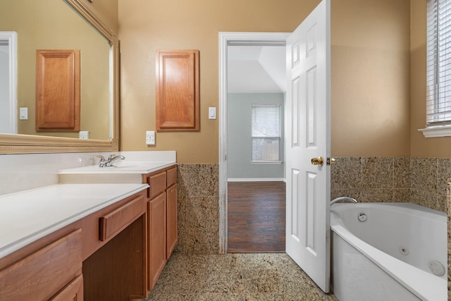 bathroom featuring a tub with jets, vanity, and a healthy amount of sunlight