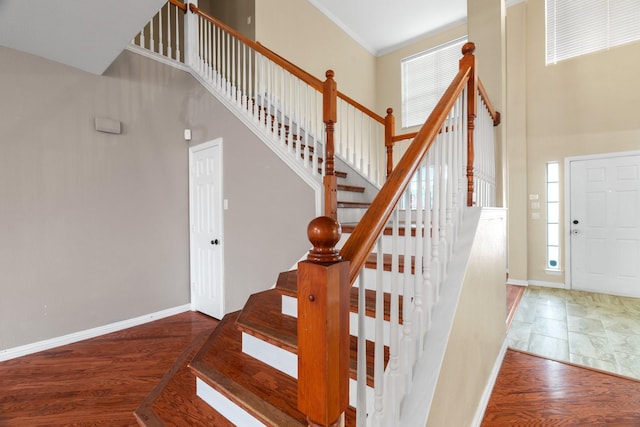 stairway with a towering ceiling, a healthy amount of sunlight, and wood finished floors