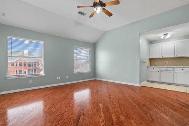 unfurnished living room featuring visible vents, light wood-style floors, vaulted ceiling, ceiling fan, and baseboards