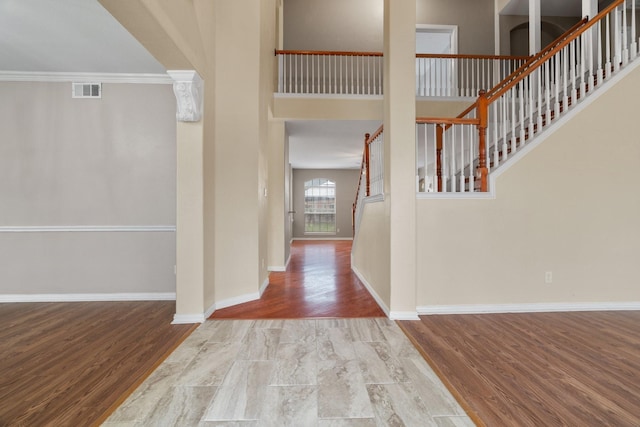 foyer entrance with baseboards, wood finished floors, a high ceiling, stairs, and crown molding