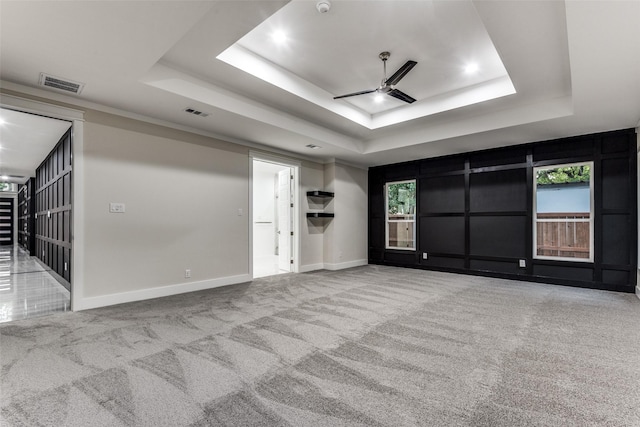 carpeted empty room with ceiling fan, a raised ceiling, visible vents, and baseboards