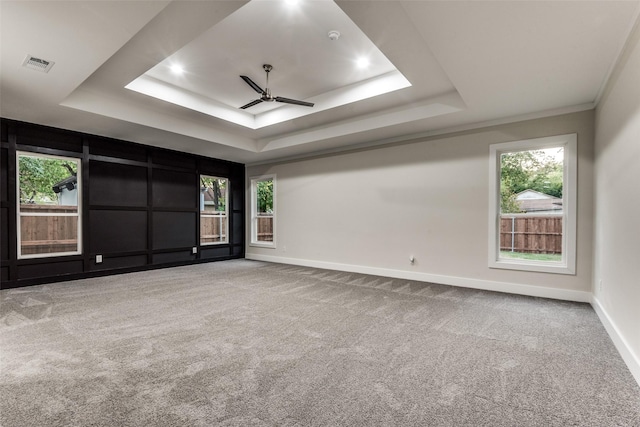 spare room with carpet, a raised ceiling, visible vents, ceiling fan, and baseboards