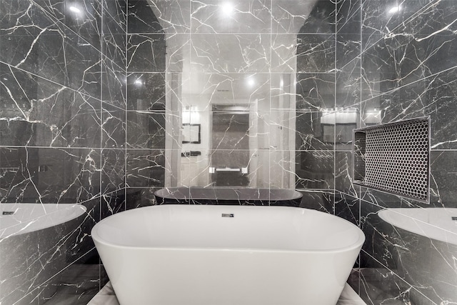 full bath with marble finish floor, tile walls, and a soaking tub