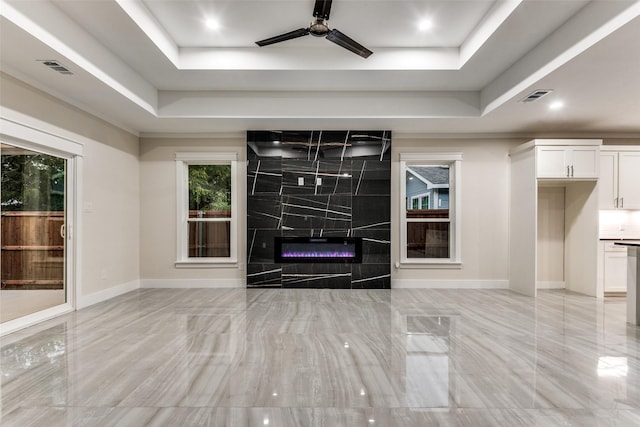 unfurnished living room featuring visible vents, a fireplace, a tray ceiling, and ceiling fan