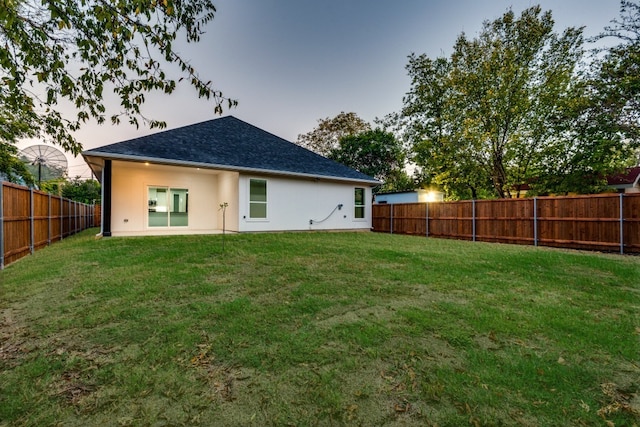 rear view of house featuring a shingled roof, a fenced backyard, a lawn, and stucco siding