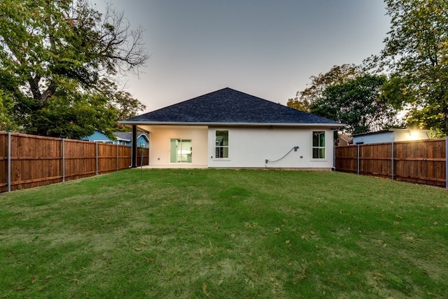 rear view of house featuring a fenced backyard, a shingled roof, and a lawn