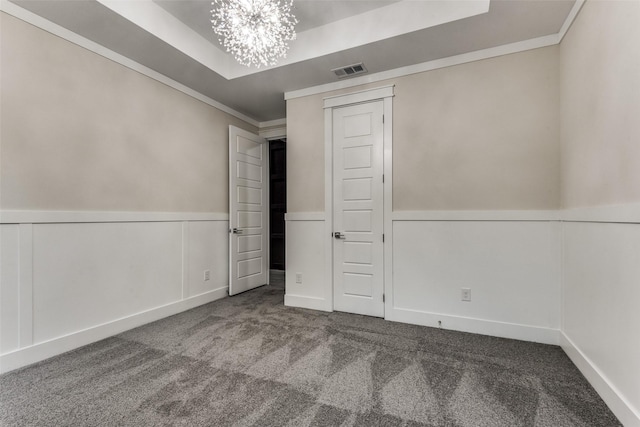 unfurnished bedroom featuring a notable chandelier, a wainscoted wall, carpet floors, visible vents, and a tray ceiling