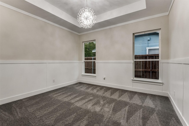 empty room with a wainscoted wall, crown molding, a notable chandelier, dark colored carpet, and a raised ceiling