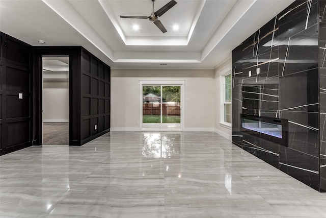 spare room with marble finish floor, ceiling fan, baseboards, and a raised ceiling