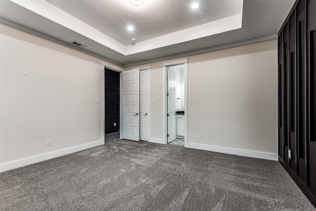 unfurnished bedroom featuring a tray ceiling, visible vents, dark carpet, and baseboards