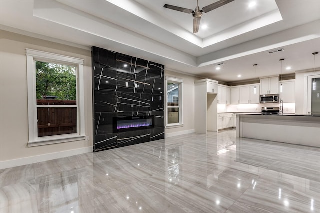 unfurnished living room featuring a high end fireplace, baseboards, visible vents, a ceiling fan, and a raised ceiling