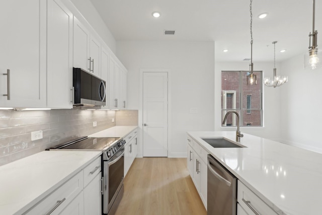 kitchen featuring tasteful backsplash, stainless steel appliances, light countertops, white cabinetry, and a sink