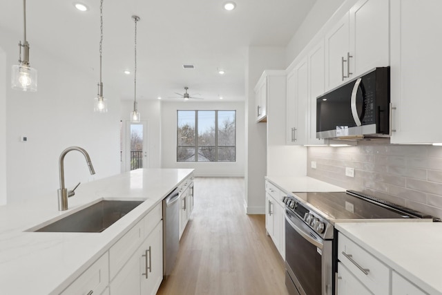 kitchen featuring tasteful backsplash, appliances with stainless steel finishes, light wood-style floors, white cabinetry, and a sink