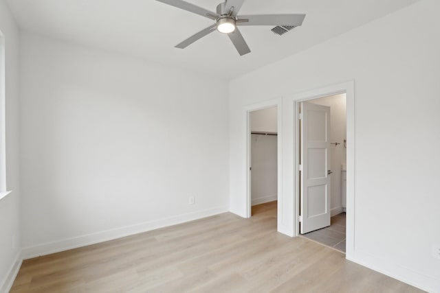 unfurnished bedroom featuring light wood-style flooring, visible vents, baseboards, a closet, and a walk in closet