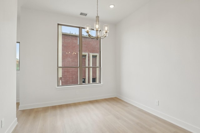 spare room featuring baseboards, light wood-type flooring, visible vents, and a notable chandelier