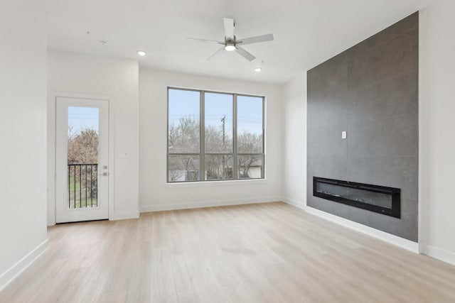 unfurnished living room featuring a ceiling fan, a fireplace, baseboards, and wood finished floors