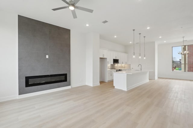 unfurnished living room featuring a fireplace, recessed lighting, visible vents, light wood-style flooring, and ceiling fan with notable chandelier