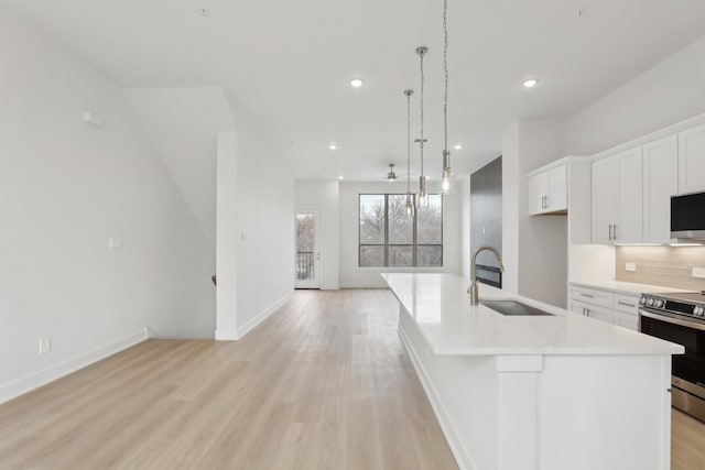 kitchen with a sink, open floor plan, light countertops, stainless steel electric range oven, and an island with sink