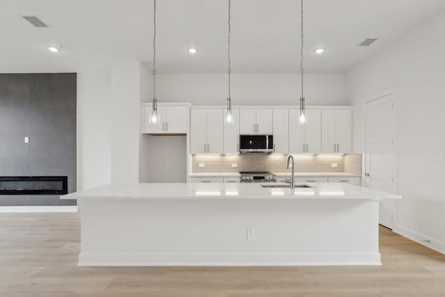 kitchen with a kitchen island with sink, a sink, visible vents, white cabinets, and appliances with stainless steel finishes