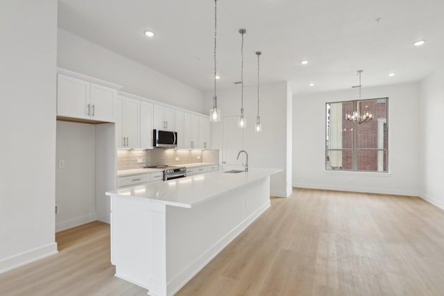 kitchen with tasteful backsplash, white cabinets, appliances with stainless steel finishes, light wood-type flooring, and a sink