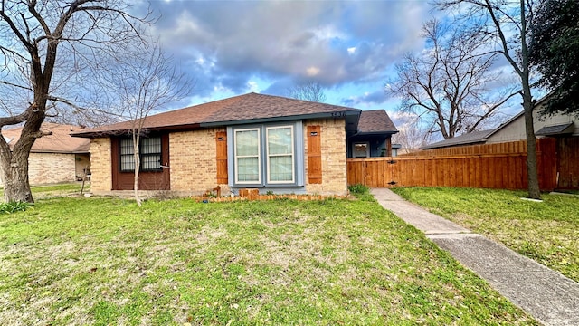 exterior space featuring a shingled roof, fence, a lawn, and brick siding