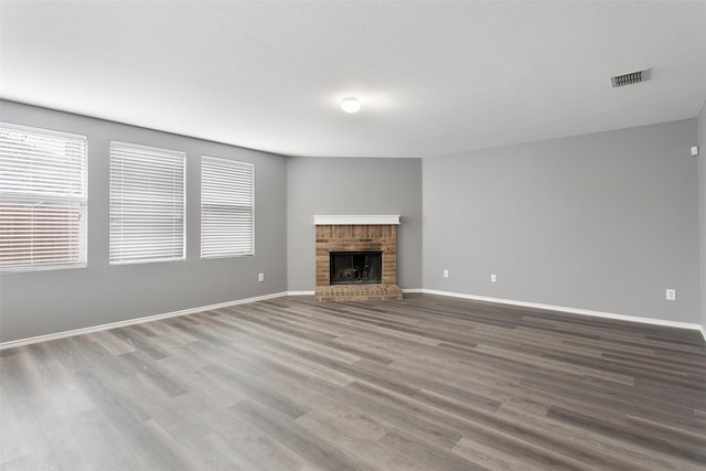 unfurnished living room featuring visible vents, a brick fireplace, baseboards, and wood finished floors