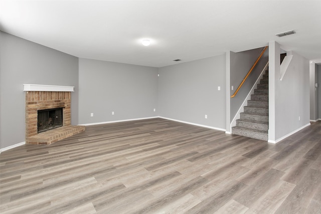 unfurnished living room featuring visible vents, a brick fireplace, stairs, and wood finished floors