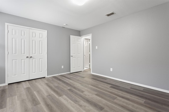 unfurnished bedroom featuring visible vents, baseboards, a closet, and wood finished floors