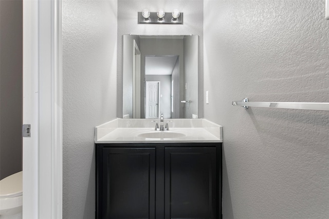 half bath with toilet, vanity, and a textured wall