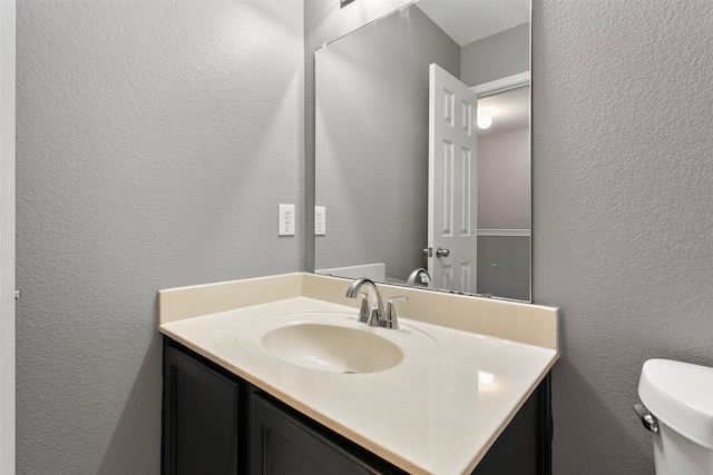 half bathroom with toilet, vanity, and a textured wall