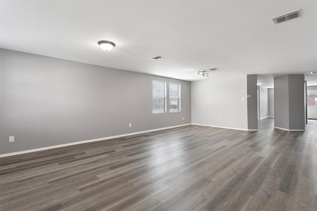 empty room with visible vents, baseboards, dark wood finished floors, and rail lighting