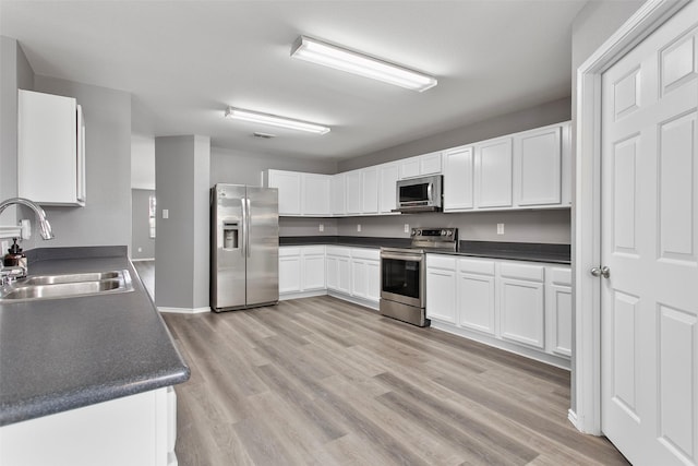 kitchen with white cabinets, appliances with stainless steel finishes, light wood-style floors, and a sink