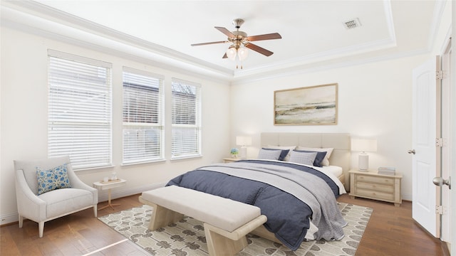 bedroom with crown molding, a raised ceiling, visible vents, a ceiling fan, and wood finished floors