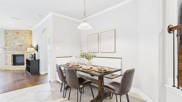 dining space with baseboards, arched walkways, ornamental molding, a stone fireplace, and light tile patterned flooring