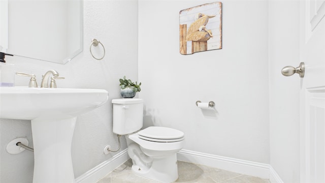 half bath with a sink, tile patterned floors, toilet, and baseboards