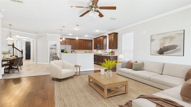 living area with arched walkways, visible vents, crown molding, and light wood-style flooring