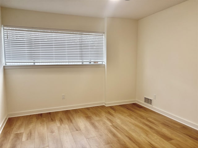 empty room featuring light wood-style floors, a wealth of natural light, visible vents, and baseboards