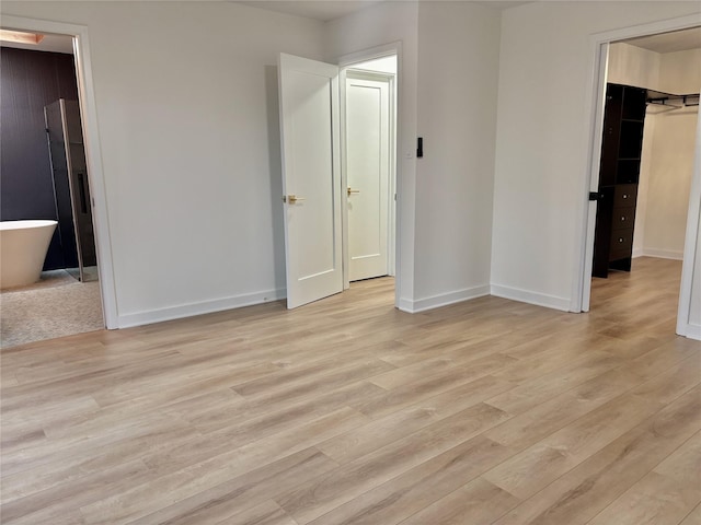 unfurnished bedroom featuring a walk in closet, baseboards, and light wood finished floors