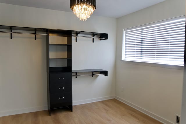 walk in closet with light wood-type flooring and an inviting chandelier