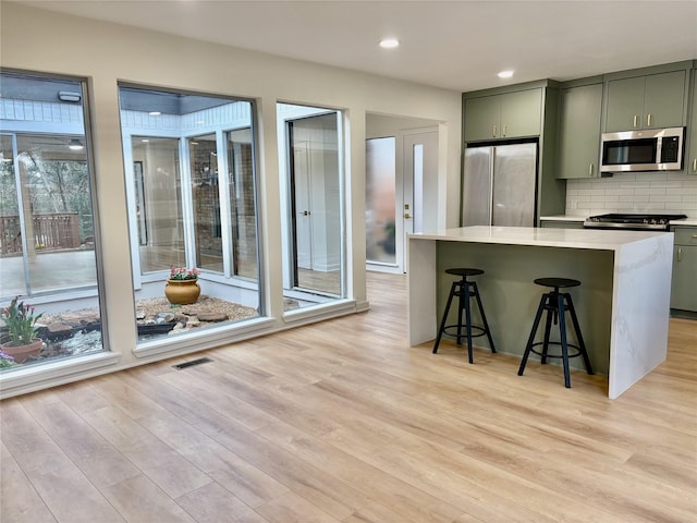 kitchen with tasteful backsplash, visible vents, light wood-style flooring, stainless steel appliances, and light countertops