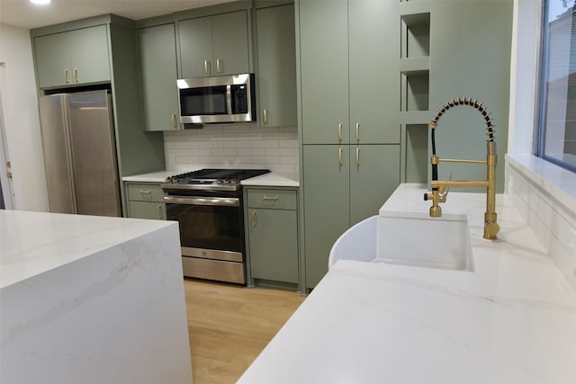 kitchen with decorative backsplash, green cabinets, stainless steel appliances, light wood-style floors, and open shelves