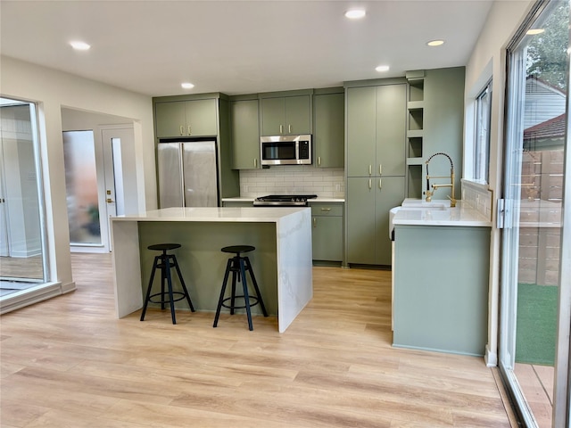 kitchen featuring light wood-type flooring, tasteful backsplash, stainless steel appliances, and green cabinetry