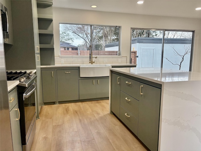 kitchen with tasteful backsplash, appliances with stainless steel finishes, light countertops, light wood-style floors, and a sink