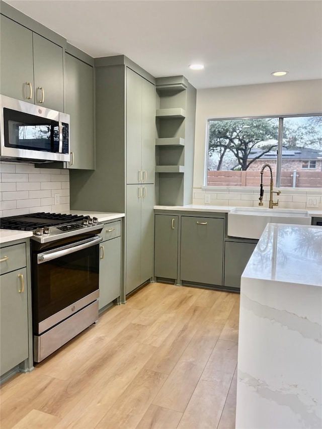 kitchen featuring tasteful backsplash, stainless steel appliances, light wood-style floors, open shelves, and a sink