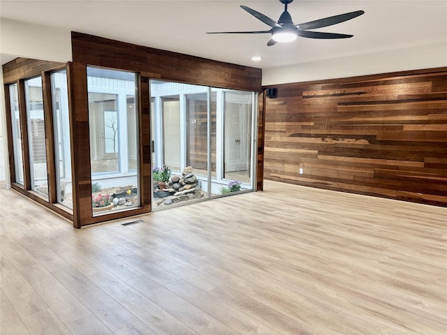 unfurnished room featuring a ceiling fan, visible vents, wood walls, and wood finished floors