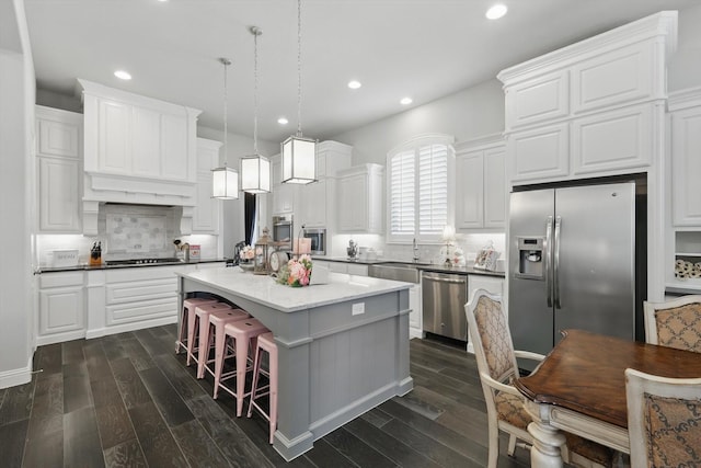 kitchen with dark wood finished floors, decorative backsplash, a kitchen island, appliances with stainless steel finishes, and white cabinetry