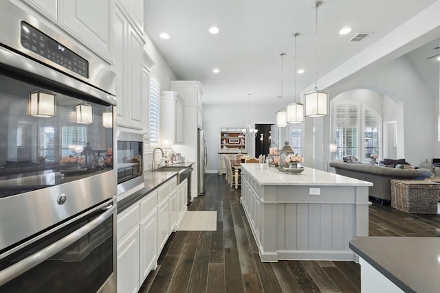 kitchen featuring arched walkways, dark wood finished floors, stainless steel appliances, visible vents, and open floor plan