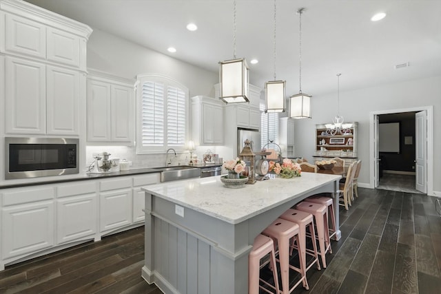 kitchen with a sink, a kitchen breakfast bar, appliances with stainless steel finishes, a center island, and dark wood-style floors