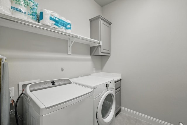 washroom featuring cabinet space, washing machine and dryer, baseboards, and light tile patterned flooring