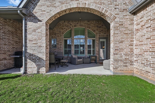 property entrance featuring brick siding, a lawn, and a patio